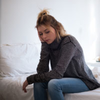 woman sitting on the edge of her bed looking down, sad