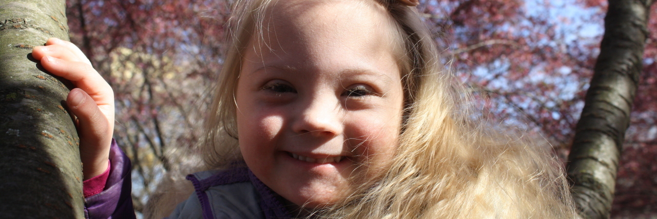 Helping My Child With Down Syndrome Develop at Her Own Pace Farah's daughter outdoors with colorful trees in the background.
