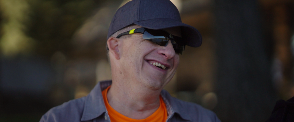 Mike Barnett, a white man wearing a blue ball cap and sunglasses, smiling