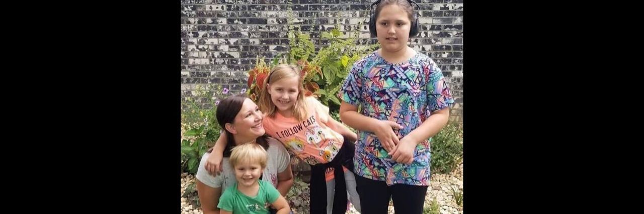 Please Don't Judge How I Care for My Autistic Daughter a mother posing for a picture on the grass with her three children.