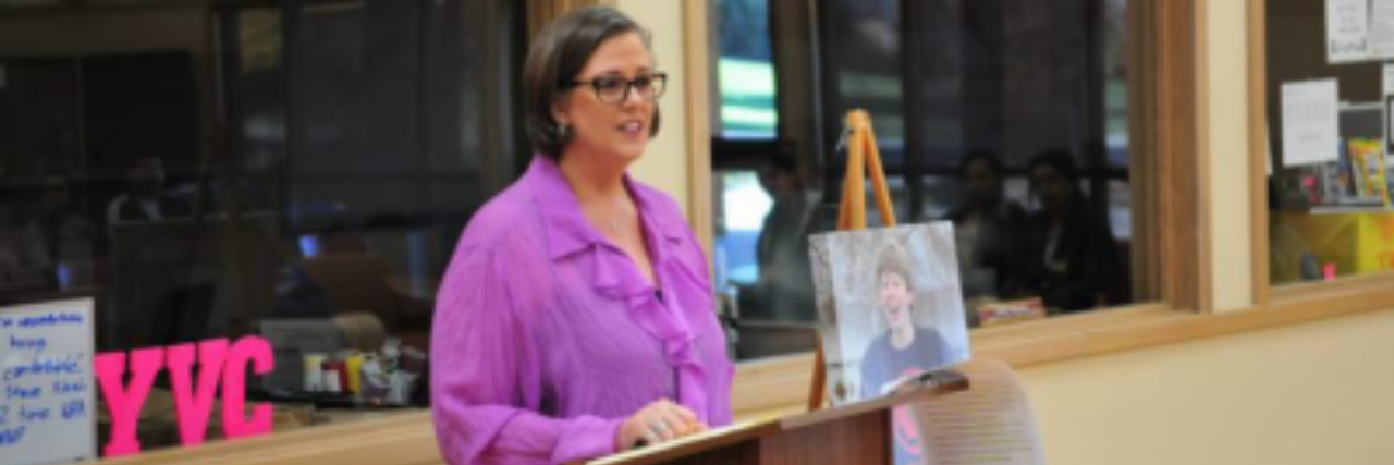 How Losing My Son to Suicide Has Had Far-Reaching, Lifesaving Impacts author standing behind a podium with a picture of her son to her left
