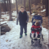 A young boy and his sibling who's in a stroller. They're outside in the snow
