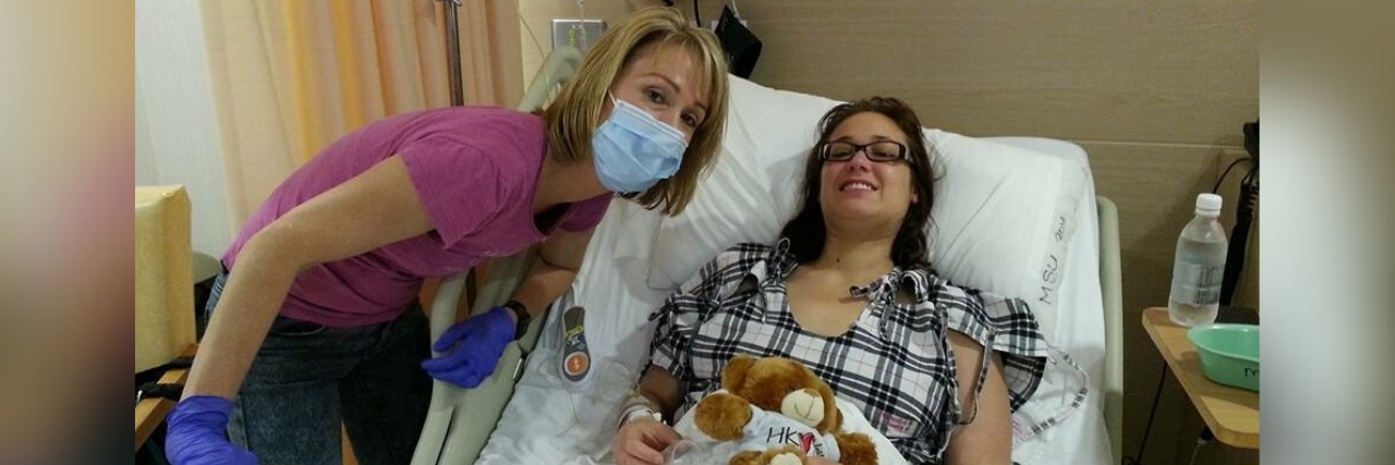 The author laying in a hospital bed with her mom standing next to her. Her mom is wearing a face mask.