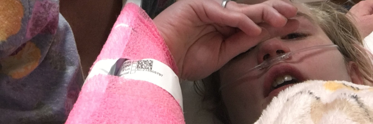 What Getting Tested for COVID-19 Was Like as a Trauma Survivor photo from contributor showing her lying in hospital with blonde woman wearing glasses and hospital mask nearby