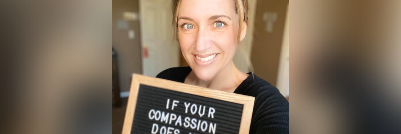 author holding a sign saying "if your compassion does not include yourself it is incomplete."