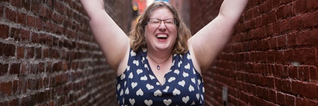 Interview: What Body Positivity Icon Lindley Ashline Wants You to Know About Your Self-Image photo of Lindley Ashline, body positive icon and owner of Body Liberation Stock and The Body Love Box. She is seen in an alley, smiling with her eyes closed and raising her arms high
