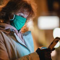 photo of woman in illness mask looking at phone