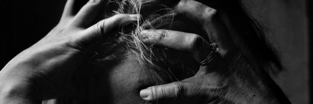 A closeup of a woman holding her hands over the top of her head. Black and white photo.