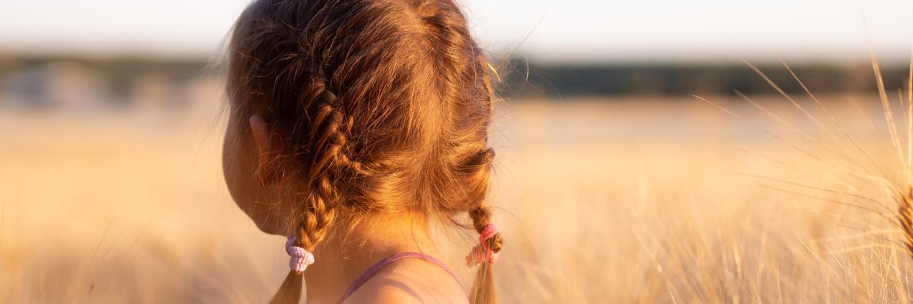 young girl with red braids standing in a field with her back to the camera