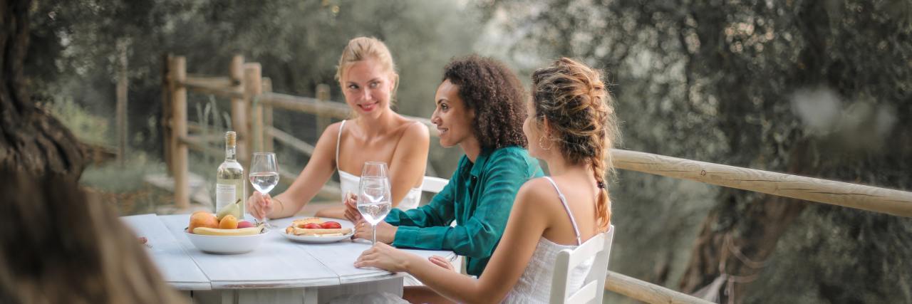 photo of three women at table outside, eating and talking