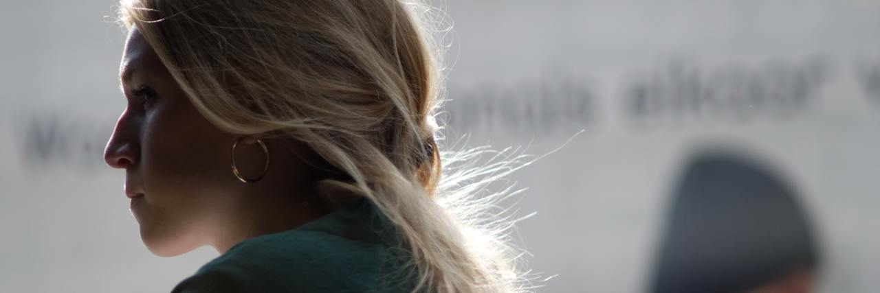 woman with blonde hair in a green sweater sitting at a desk with a straight face