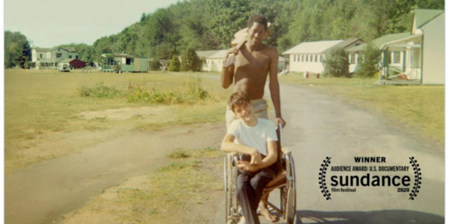Crip Camp poster showing a vintage image of a man pushing another man in a wheelchair.