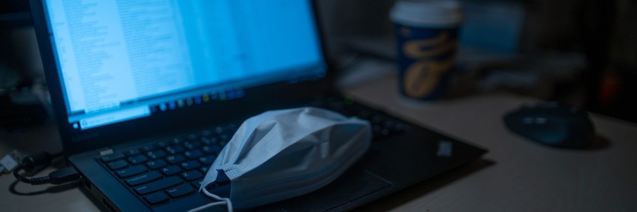 Open laptop computer with a surgical mask lying on the keyboard