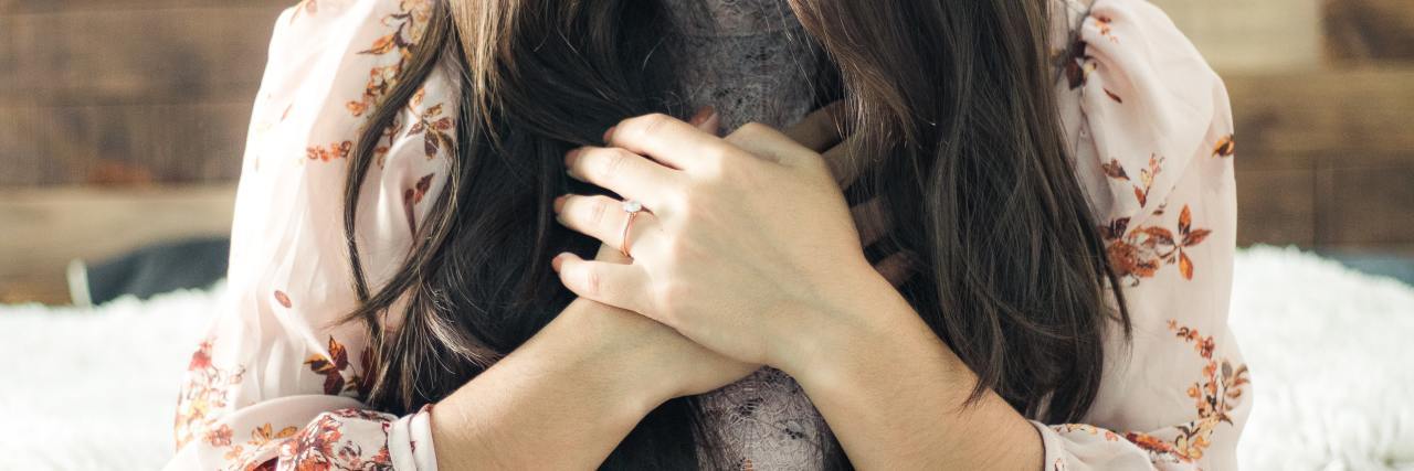 How to Spread Kindness While Anxious About the Coronavirus photo of woman with long hair and flowery top, her hands clasped to her chest