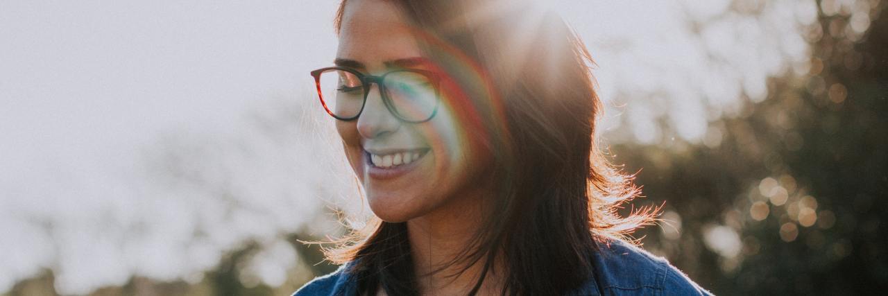 Why You Should Check In on Your 'Happy' Friends With Depression photo of woman looking happy with eyes closed and sunlight shining on her face in a lens flare