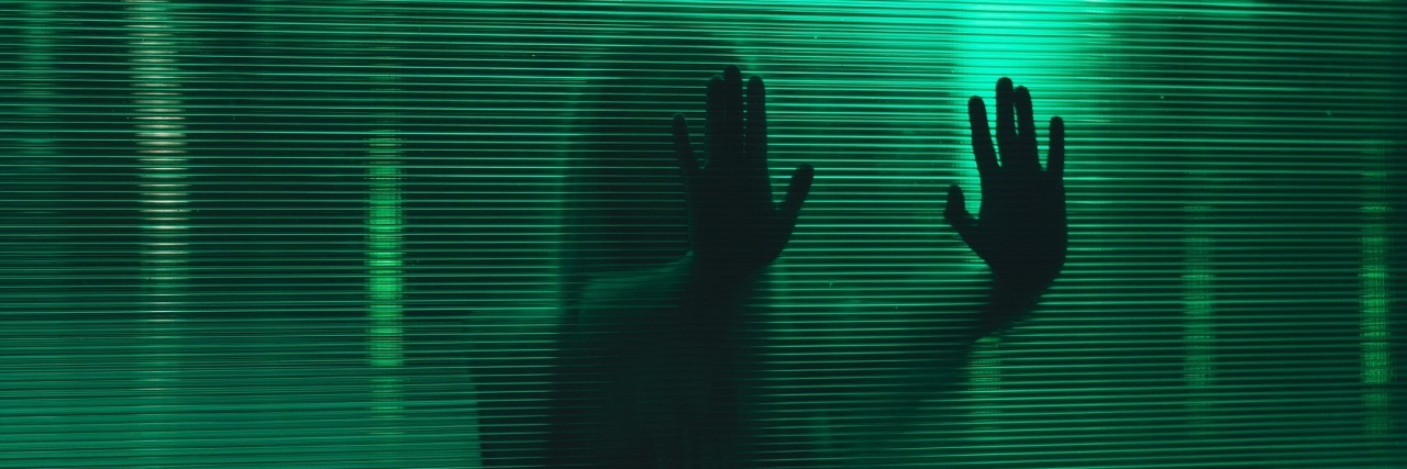 photo of woman behind glass and silhouetted by green light, pressing hands to glass