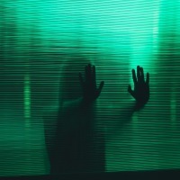 photo of woman behind glass and silhouetted by green light, pressing hands to glass