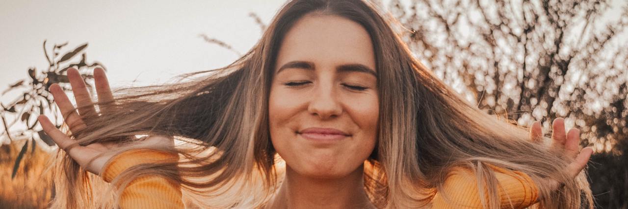 8 Ways to Help Get Your Happiness Back on Track and Thrive woman in an orange shirt, smiling with her eyes closed holding her brown hair