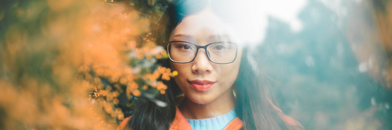 The Isolation of Being Asian While COVID-19 Racism Is Rampant woman with glasses peeking through trees