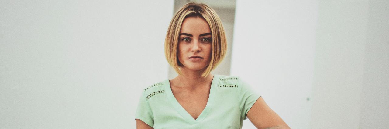 I'm Not 'Weak' Because of My Anxiety, Despite the Friends Who Left Me woman in a green v-neck resting her arm on a chair staring seriously into the camera