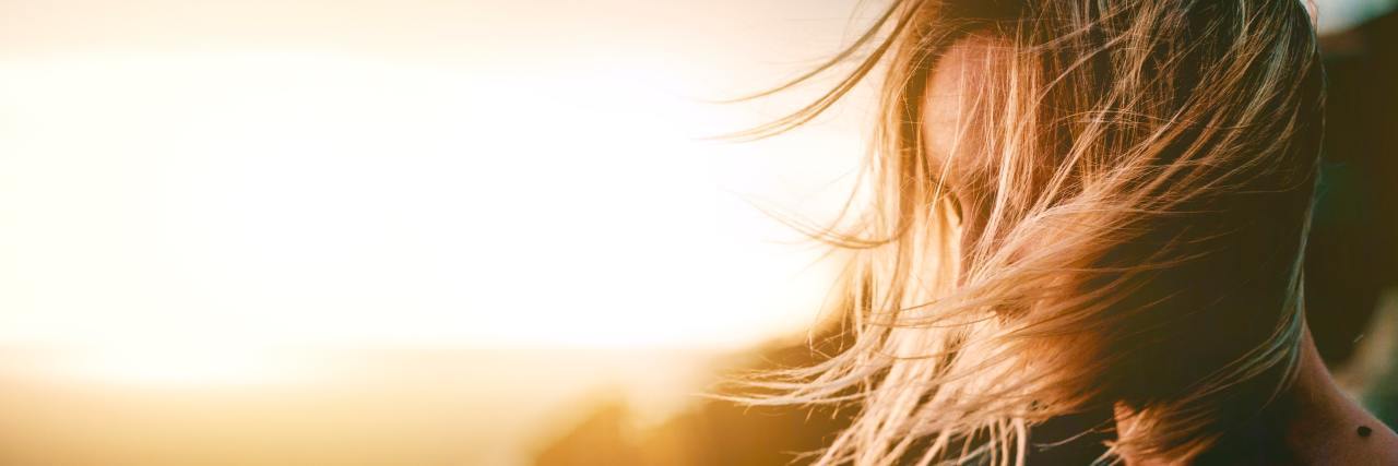 Why It's OK I'm Healing and Recovering From Trauma at My Own Pace woman standing on a mountain with the sun shining, her hair blowing over her face