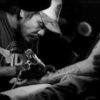 black and white photo of man tattooing a client's arm
