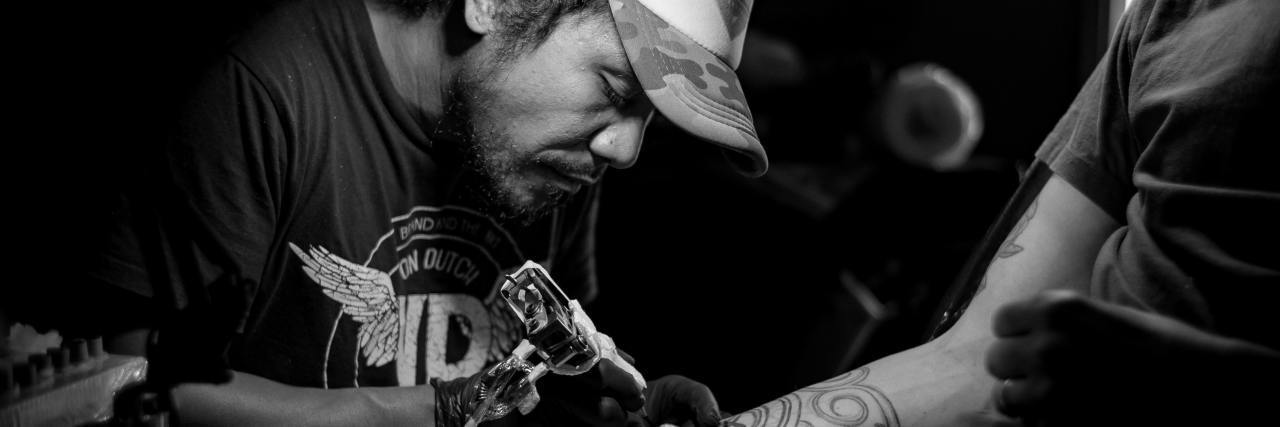 Getting a Tattoo to Cover Self-Harm Scars black and white photo of man tattooing a client's arm