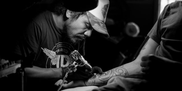 black and white photo of man tattooing a client's arm