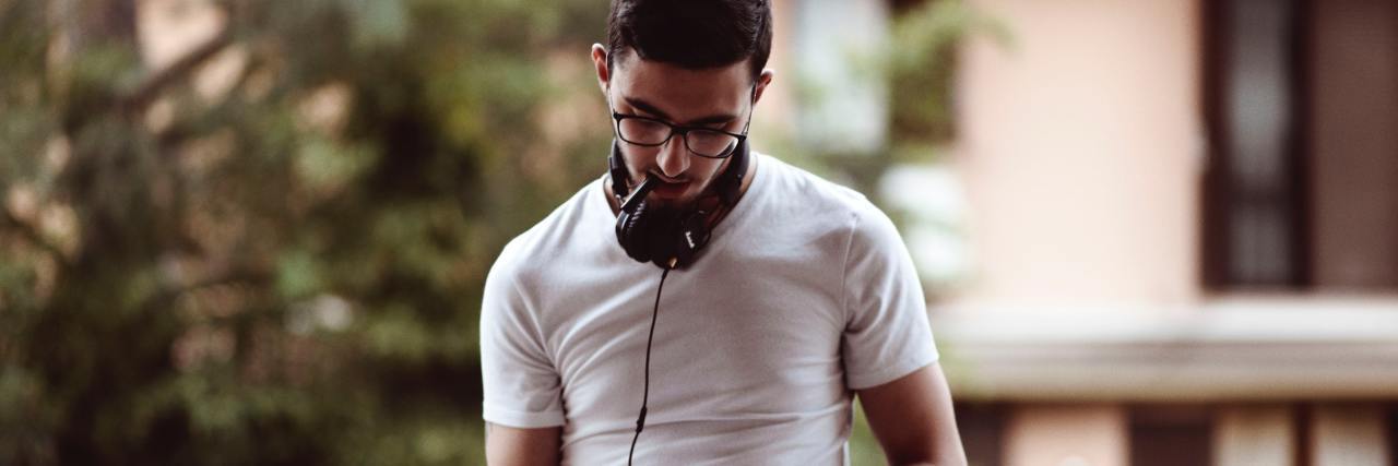 3 Reasons Tracking My Moods Isn't Helpful for Me as Someone With OCD man in white t-shirt with headphones around his neck, writing in a journal while standing outside on a balcony