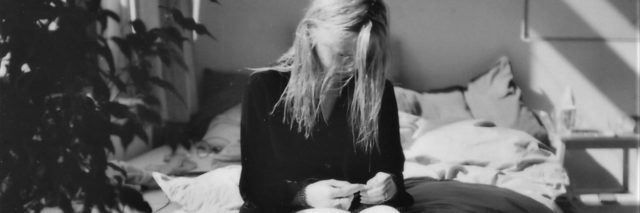black and white photo of woman sitting on bed looking down with face partly hidden by hair