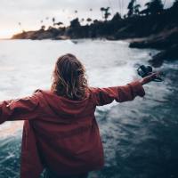 photo of woman standing by shore with outstretched arms