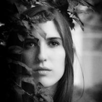 black and white photo of a woman with a straight face looking ahead through leaves/bushes
