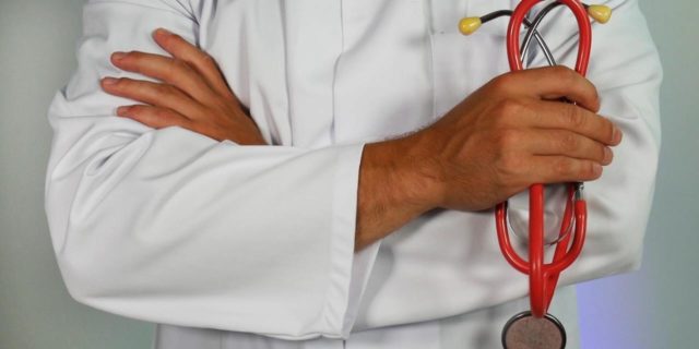 Doctor in a white lab coat, arms only, holding a red stethoscope