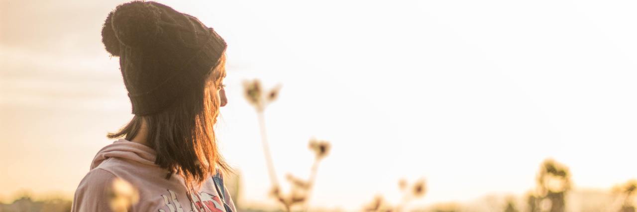I May Feel Hopeless in My Fight With PTSD, but I Am Not Helpless woman in a beanie standing outside in a field with flowers