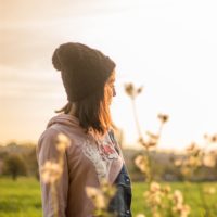 woman in a beanie standing outside in a field with flowers