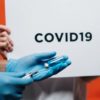 A health care worker fills a syringe from a vial in front of a sign that says COVID-19