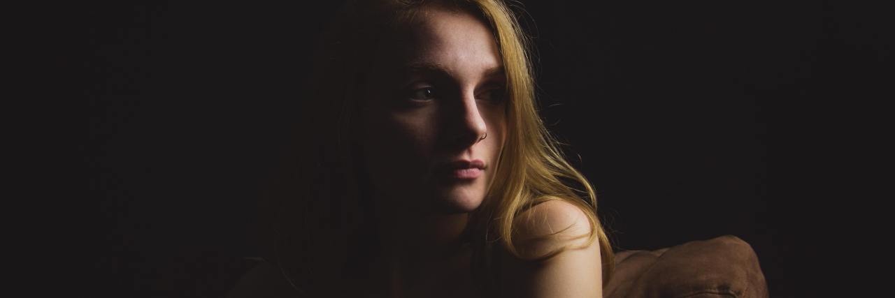 When Negative Self-Talk Looks Like Emotional Abuse Toward Yourself photo of woman in darkness and light cast on her from one direction, looking sad off-camera