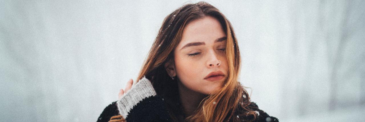9 Tips for Fighting Seasonal Depression This Winter woman standing outside in the snow with her eyes closed and hand running through her hair