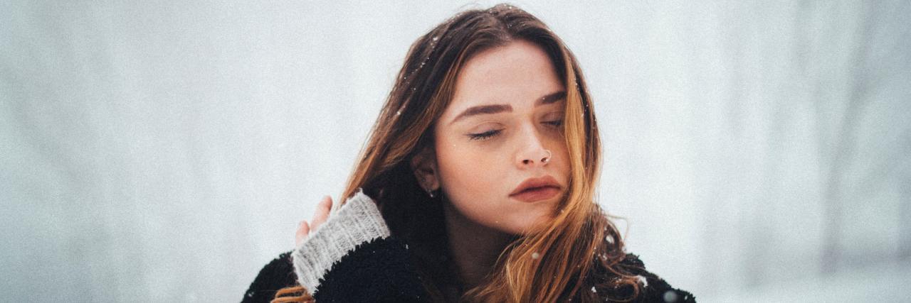 woman standing outside in the snow with her eyes closed and hand running through her hair