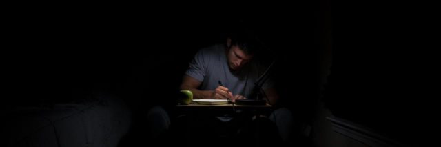 man in a blue shirt writing at a desk in the dark