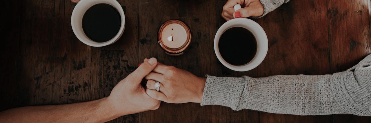A couple holding hands over a table with coffee mugs and a candle