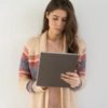 photo of young woman with large tablet computer standing against white wall