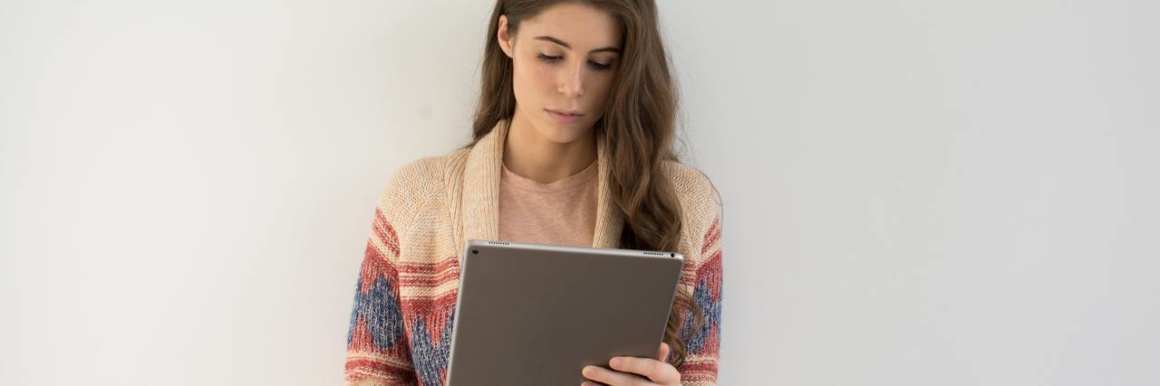 photo of young woman with large tablet computer standing against white wall