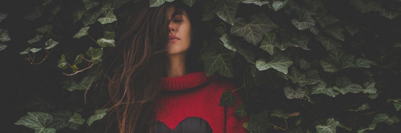 photo of woman standing with her back to ivy and her eyes closed, wearing a red heart sweater