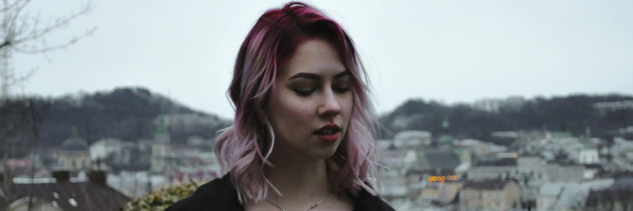 woman with pink hair standing on a mountain looking away