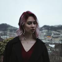 woman with pink hair standing on a mountain looking away
