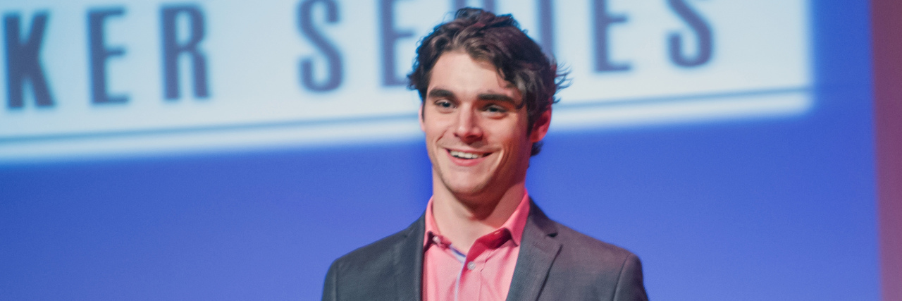 RJ Mitte Calls Out Assumption People Often Make About Disabilities RJ Mitte speaks onstage in a grey suit at an event