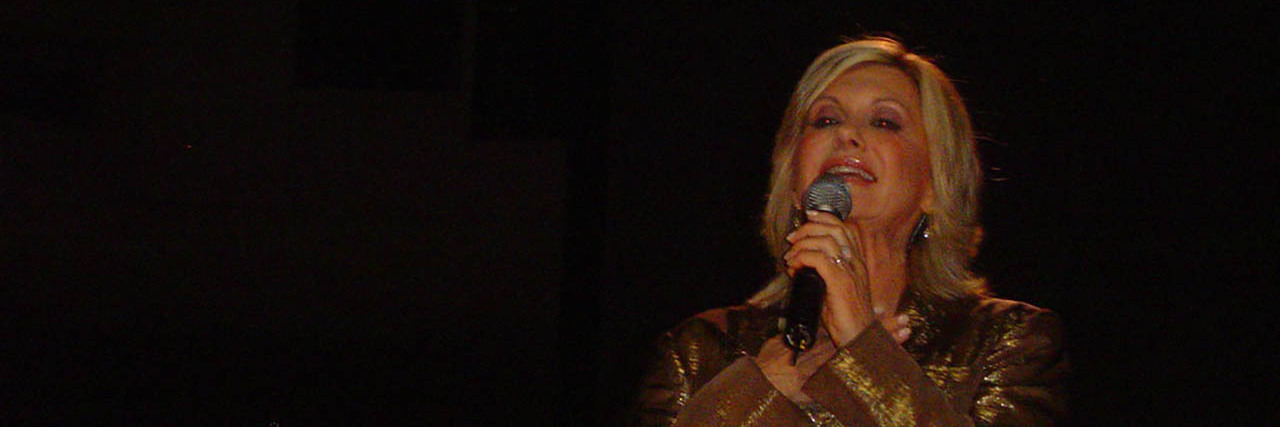 Olivia Newton-John Shares Why She Doesn't Know Cancer Prognosis Olivia Newton-John performs onstage in a gold ensemble