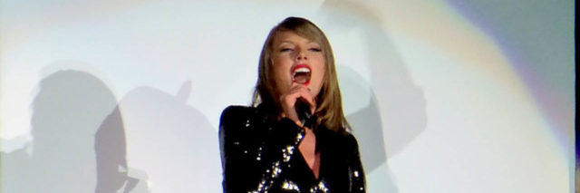 Taylor Swift performs onstage while wearing a black ensemble