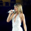 Taylor Swift performs onstage while wearing a white ensemble